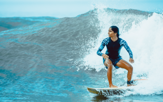 Moda Praia nos Jogos Olímpicos de Paris: estilo e performance | Foto de mulher surfando com roupa de banho