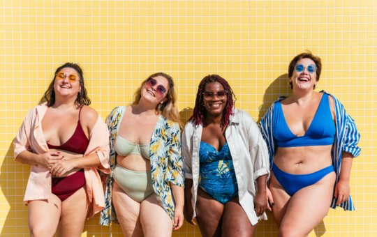 A moda praia plus size em ascensão | Quatro mulheres plus sizes sorrindo vestindo roupas de banho